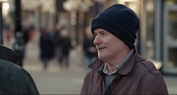 Movie still from “I, Daniel Blake” (2016), directed by Ken Loach – A person wearing a jacket and a hat; Close Up shot, Over the shoulder angle