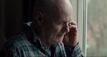 Movie still from “I, Daniel Blake” (2016), directed by Ken Loach – An older bald man is holding his head down and talking on a cell phone; Close Up shot, Low angle