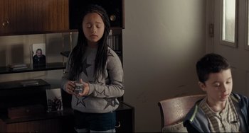 Movie still from “I, Daniel Blake” (2016), directed by Ken Loach – A young girl holding a camera in a room; Medium shot, Over the shoulder angle