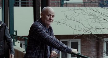 Movie still from “I, Daniel Blake” (2016), directed by Ken Loach – An older man sitting on top of a railing; Medium shot, Low angle