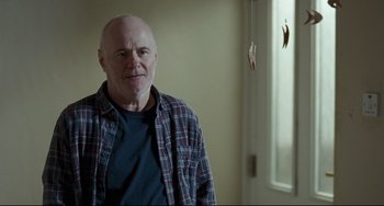 Movie still from “I, Daniel Blake” (2016), directed by Ken Loach – An older man standing in front of a window; Medium shot, Over the shoulder angle