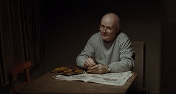 Movie still from “I, Daniel Blake” (2016), directed by Ken Loach – An older man sitting at a table with a newspaper; Medium shot, High angle