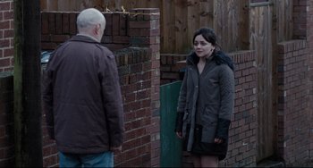 Movie still from “I, Daniel Blake” (2016), directed by Ken Loach – A woman standing next to an older man in front of a brick wall; Medium shot, Over the shoulder angle