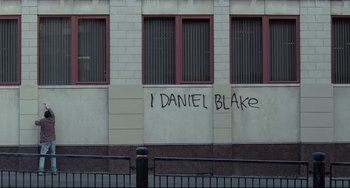 Movie still from “I, Daniel Blake” (2016), directed by Ken Loach – Graffiti on a building on a city street; Extreme Wide shot, High angle