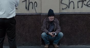 Movie still from “I, Daniel Blake” (2016), directed by Ken Loach – A man sitting on the ground with a cell phone; Wide shot, Low angle