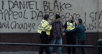 Movie still from “I, Daniel Blake” (2016), directed by Ken Loach – A group of people standing next to each other on the street; Medium shot, Over the shoulder angle