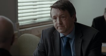 Movie still from “I, Daniel Blake” (2016), directed by Ken Loach – A person wearing a suit and tie; Close Up shot, Over the shoulder angle