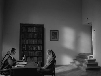 Movie still from “Ida” (2013), directed by Pawel Pawlikowski – A nun sitting at a table in a room with books; Wide shot, Low angle