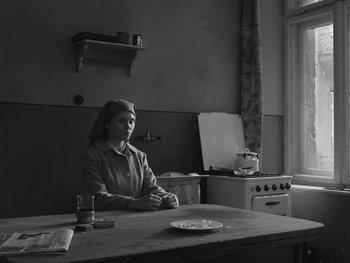 Movie still from “Ida” (2013), directed by Pawel Pawlikowski – A woman sitting at a table in front of an oven in a kitchen; Medium shot, High angle