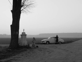 Movie still from “Ida” (2013), directed by Pawel Pawlikowski – A woman standing next to a car on a dirt road; Wide shot, High angle