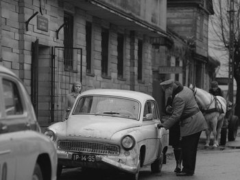 Movie still from “Ida” (2013), directed by Pawel Pawlikowski – An old photo of two people looking at an old car on the side of the street; Wide shot, High angle