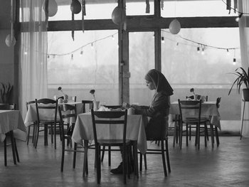 Movie still from “Ida” (2013), directed by Pawel Pawlikowski – A woman sitting at a table in front of a large window; Wide shot, Low angle
