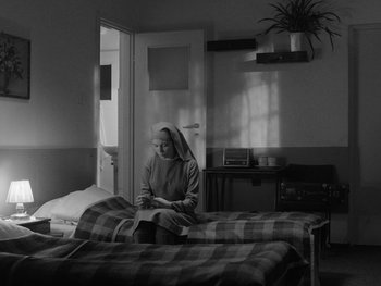 Movie still from “Ida” (2013), directed by Pawel Pawlikowski – A nun sitting on a bed in a room; Wide shot, High angle