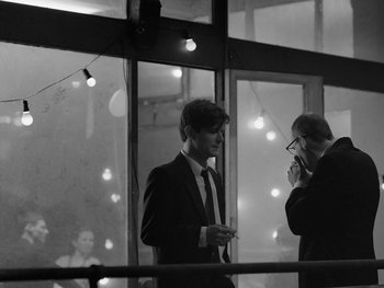 Movie still from “Ida” (2013), directed by Pawel Pawlikowski – Two men in suits and ties standing next to each other in front of a window; Medium shot, Over the shoulder angle