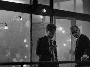 Movie still from “Ida” (2013), directed by Pawel Pawlikowski – A man standing next to another man holding a cell phone; Medium shot, Over the shoulder angle