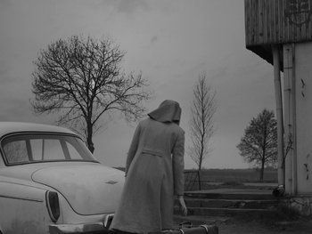 Movie still from “Ida” (2013), directed by Pawel Pawlikowski – A woman in a long coat standing in front of a car; Wide shot, Low angle
