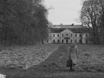 Movie still from “Ida” (2013), directed by Pawel Pawlikowski – A woman with a briefcase walking down a path in front of a house; Wide shot, Low angle