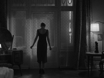 Movie still from “Ida” (2013), directed by Pawel Pawlikowski – A woman standing in front of a window in a dark room; Wide shot, Low angle