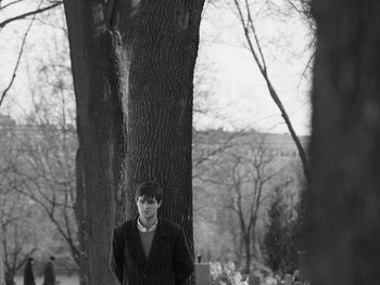 Movie still from “Ida” (2013), directed by Pawel Pawlikowski – A man standing next to a tree in a wooded area; Wide shot, Over the shoulder angle