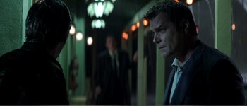 Movie still from “Identity” (2003), directed by James Mangold – A man in a suit and tie standing in front of a wall; Close Up shot, Over the shoulder angle