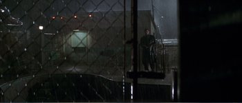 Movie still from “Identity” (2003), directed by James Mangold – A man standing in the rain holding a bag; Extreme Wide shot, High angle