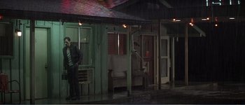 Movie still from “Identity” (2003), directed by James Mangold – A man standing in the rain next to a building; Wide shot, Low angle