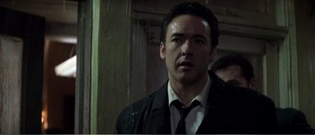 Movie still from “Identity” (2003), directed by James Mangold – A man wearing a suit and tie standing in front of a wall; Close Up shot, Low angle