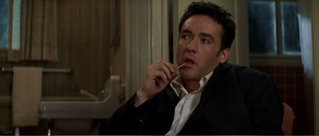 Movie still from “Identity” (2003), directed by James Mangold – A person sitting in a chair holding a pen; Close Up shot, Low angle