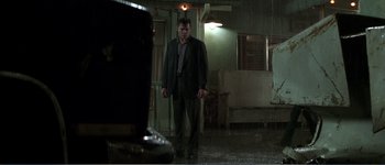 Movie still from “Identity” (2003), directed by James Mangold – A man in a suit and tie standing in a dark room; Wide shot, Low angle