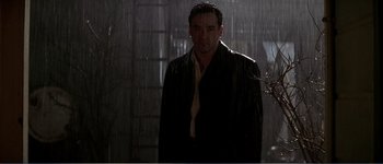 Movie still from “Identity” (2003), directed by James Mangold – A man standing in the rain wearing a jacket and tie; Medium shot, Low angle