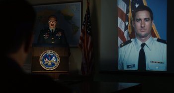 Movie still from “Idiocracy” (2006), directed by Mike Judge – A man in a military uniform standing in front of a podium; Medium shot, Over the shoulder angle