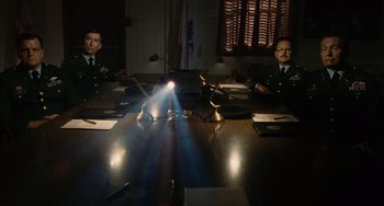 Movie still from “Idiocracy” (2006), directed by Mike Judge – Two men sitting at a conference table in front of a light; Wide shot, Low angle