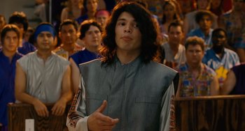 Movie still from “Idiocracy” (2006), directed by Mike Judge – A man with long black hair wearing a gray vest; Close Up shot, Over the shoulder angle