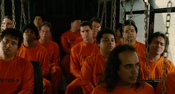 Movie still from “Idiocracy” (2006), directed by Mike Judge – A group of men in orange jumpsuits sitting in a room; Medium shot, High angle