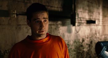 Movie still from “Idiocracy” (2006), directed by Mike Judge – A man in an orange shirt standing in a dark room; Close Up shot, Over the shoulder angle