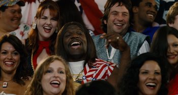 Movie still from “Idiocracy” (2006), directed by Mike Judge – A group of people sitting in front of an american flag; Medium shot, Low angle