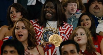 Movie still from “Idiocracy” (2006), directed by Mike Judge – A man in a patriotic outfit holding a gold medal; Medium shot, Over the shoulder angle