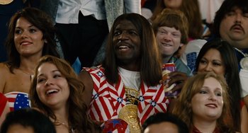 Movie still from “Idiocracy” (2006), directed by Mike Judge – A man with long black hair wearing a red , white , and blue vest; Medium shot, Over the shoulder angle