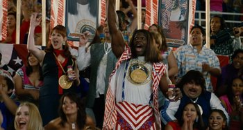 Movie still from “Idiocracy” (2006), directed by Mike Judge – A man in a red , white , and blue outfit holding up a medal; Medium shot, Low angle