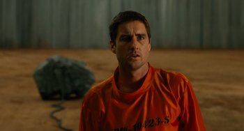 Movie still from “Idiocracy” (2006), directed by Mike Judge – A man in an orange shirt is standing in a room; Close Up shot, Over the shoulder angle