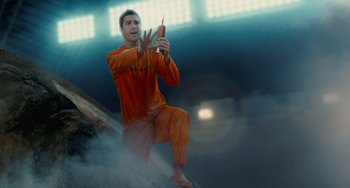 Movie still from “Idiocracy” (2006), directed by Mike Judge – A man in an orange suit is holding a cell phone; Medium shot, Low angle