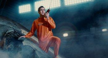 Movie still from “Idiocracy” (2006), directed by Mike Judge – A man sitting on a ledge holding a cell phone; Medium shot, Low angle