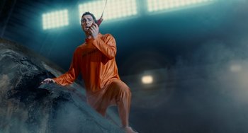 Movie still from “Idiocracy” (2006), directed by Mike Judge – A man in an orange suit is holding a cell phone; Medium shot, Low angle