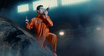 Movie still from “Idiocracy” (2006), directed by Mike Judge – A man in an orange suit is holding a cell phone; Medium shot, Low angle