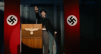 Movie still from “Idiocracy” (2006), directed by Mike Judge – A man in a suit and hat standing in front of a podium; Medium shot, Low angle