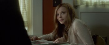 Movie still from “If I Stay” (2014), directed by R.J. Cutler – A woman sitting at a table looking at a magazine; Medium shot, Over the shoulder angle