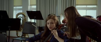 Movie still from “If I Stay” (2014), directed by R.J. Cutler – Two young women are playing the violin in a room; Medium shot, Over the shoulder angle