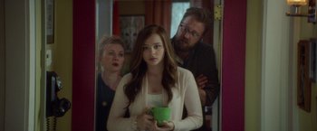 Movie still from “If I Stay” (2014), directed by R.J. Cutler – A woman holding a green cup in front of two men; Medium shot, Over the shoulder angle
