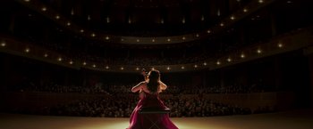 Movie still from “If I Stay” (2014), directed by R.J. Cutler – A woman in a red dress is playing the violin in front of an audience; Extreme Wide shot, High angle