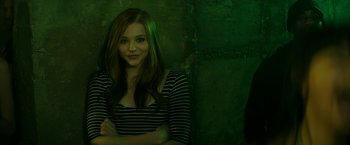 Movie still from “If I Stay” (2014), directed by R.J. Cutler – A woman standing in front of a green wall with her arms crossed; Medium shot, Low angle